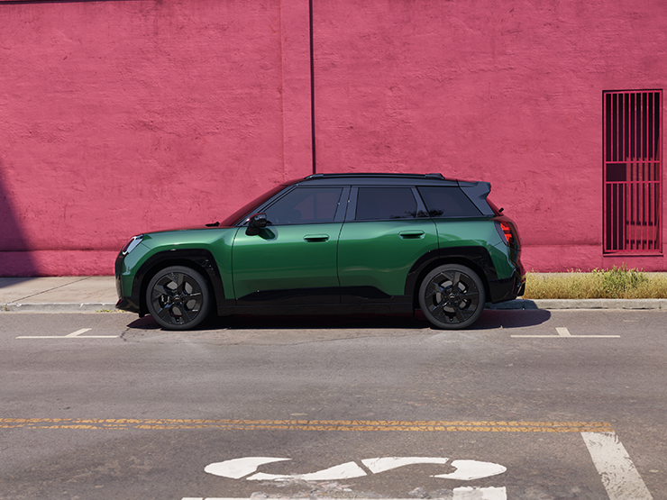 Side view of the all-electric MINI Aceman in British Racing Green and Black Roof. on a street.